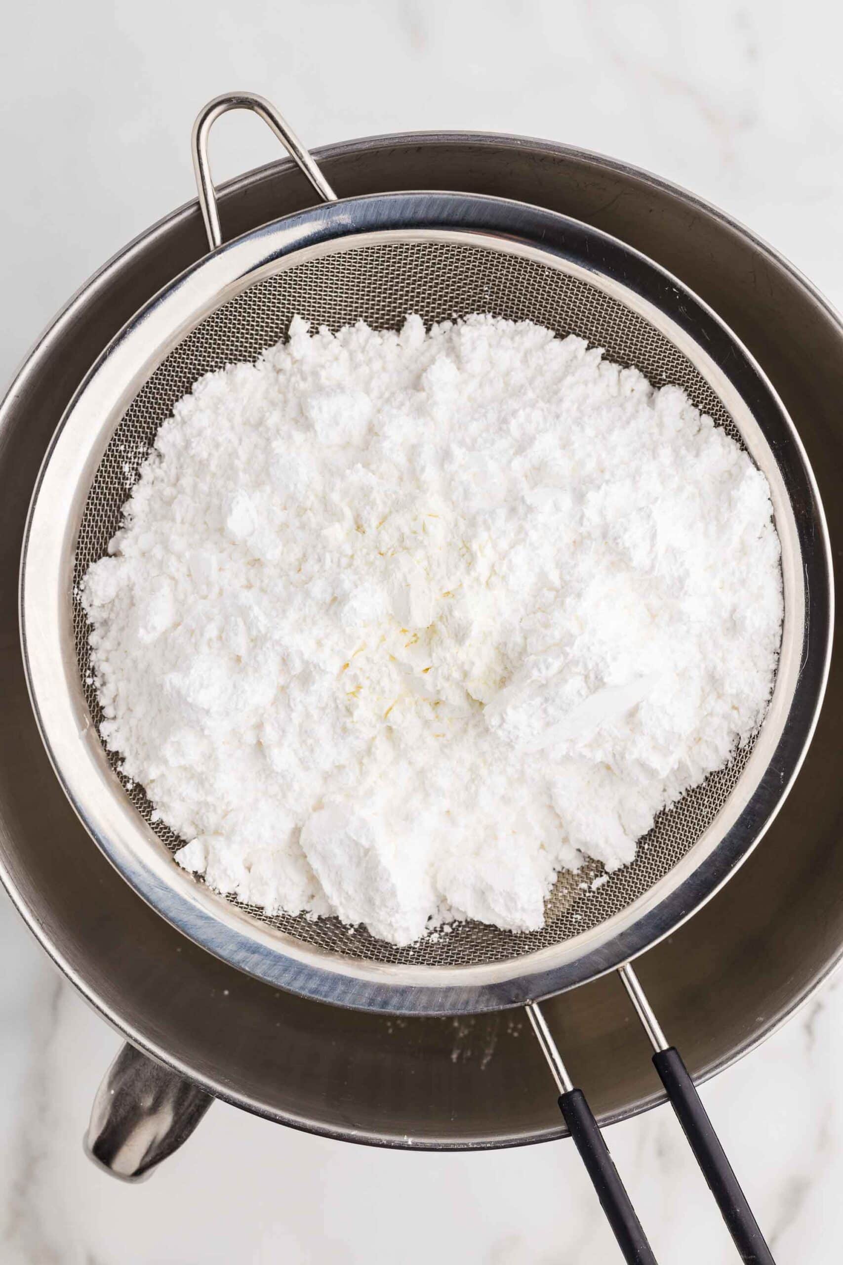 Sifting confectioners sugar over cream cheese in a stand mixer bowl