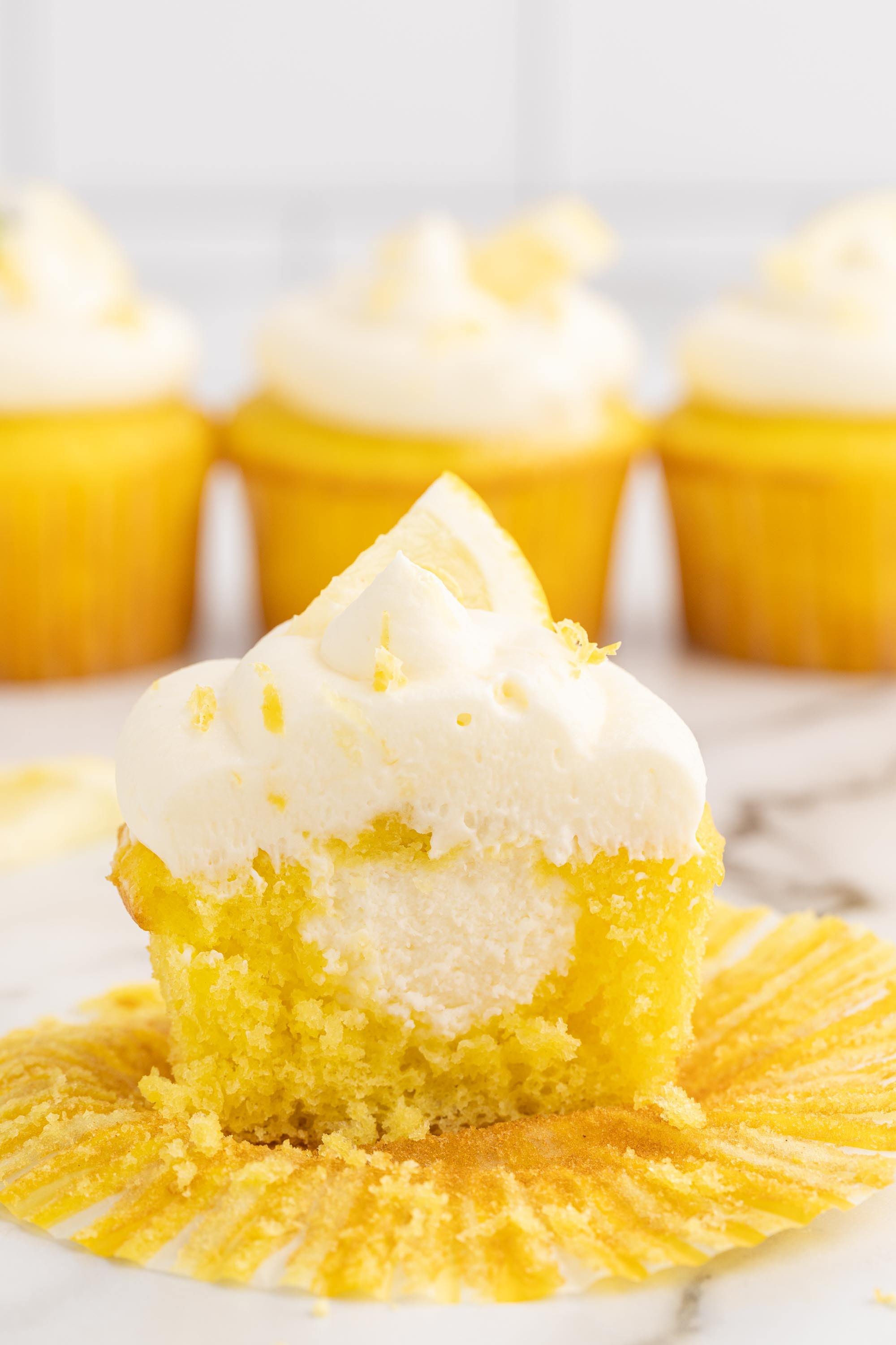 A lemon cupcake cut in half showing a center filled with lemon cheesecake filling