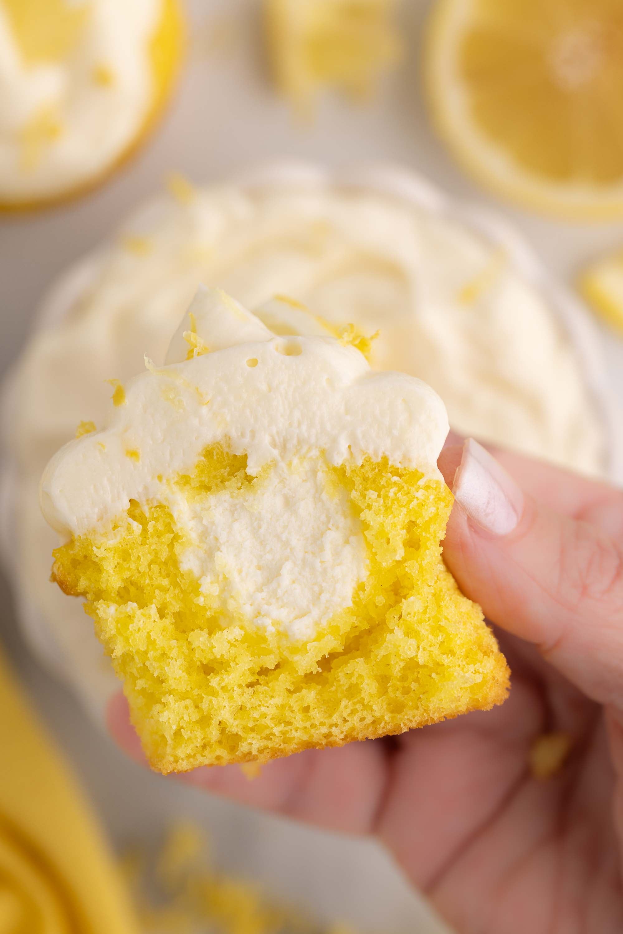A hand holding a lemon cupcake with a bite taken out, showing the lemon cheesecake filling inside