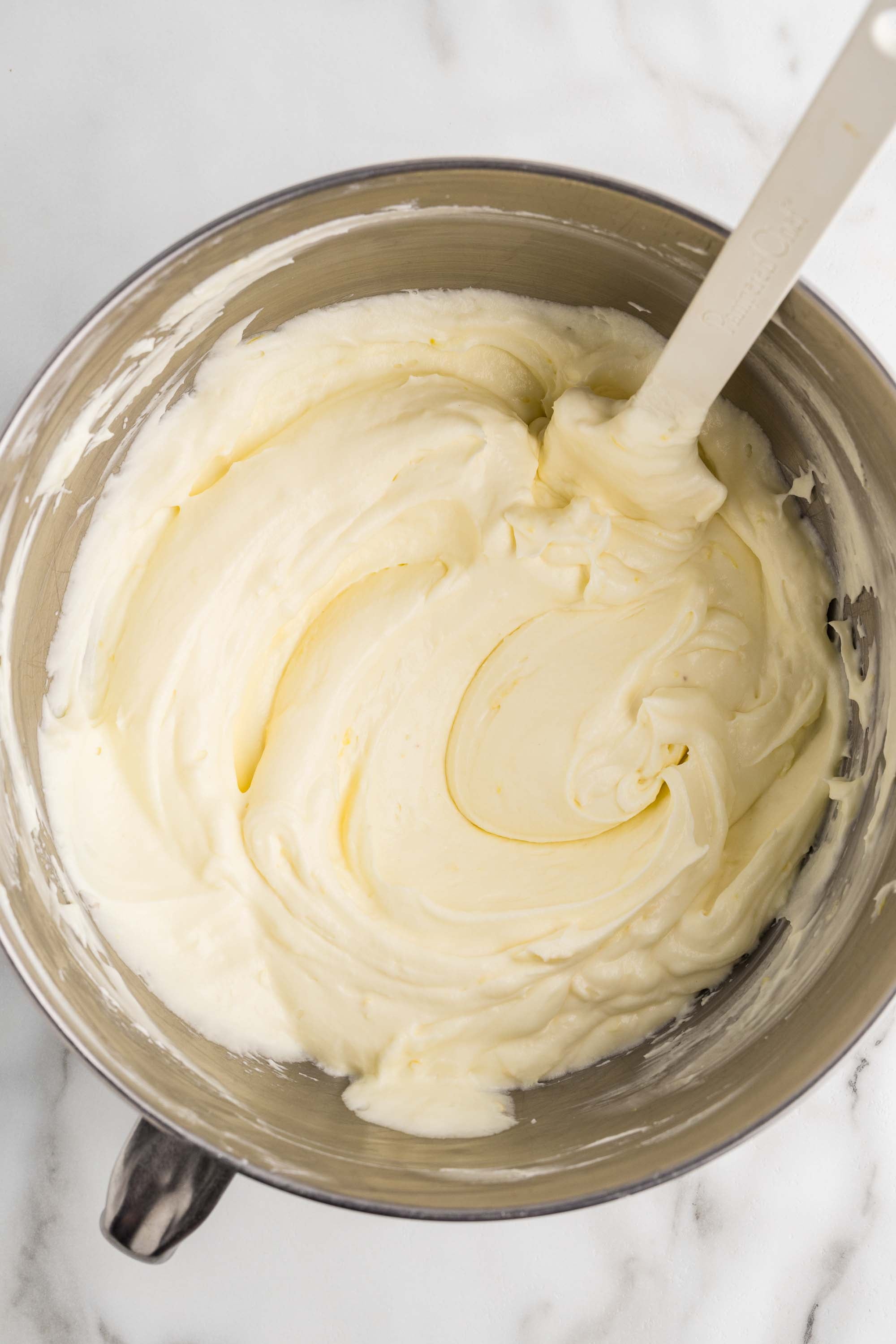 Finished lemon cheesecake filling in a stand mixer bowl with a spatula